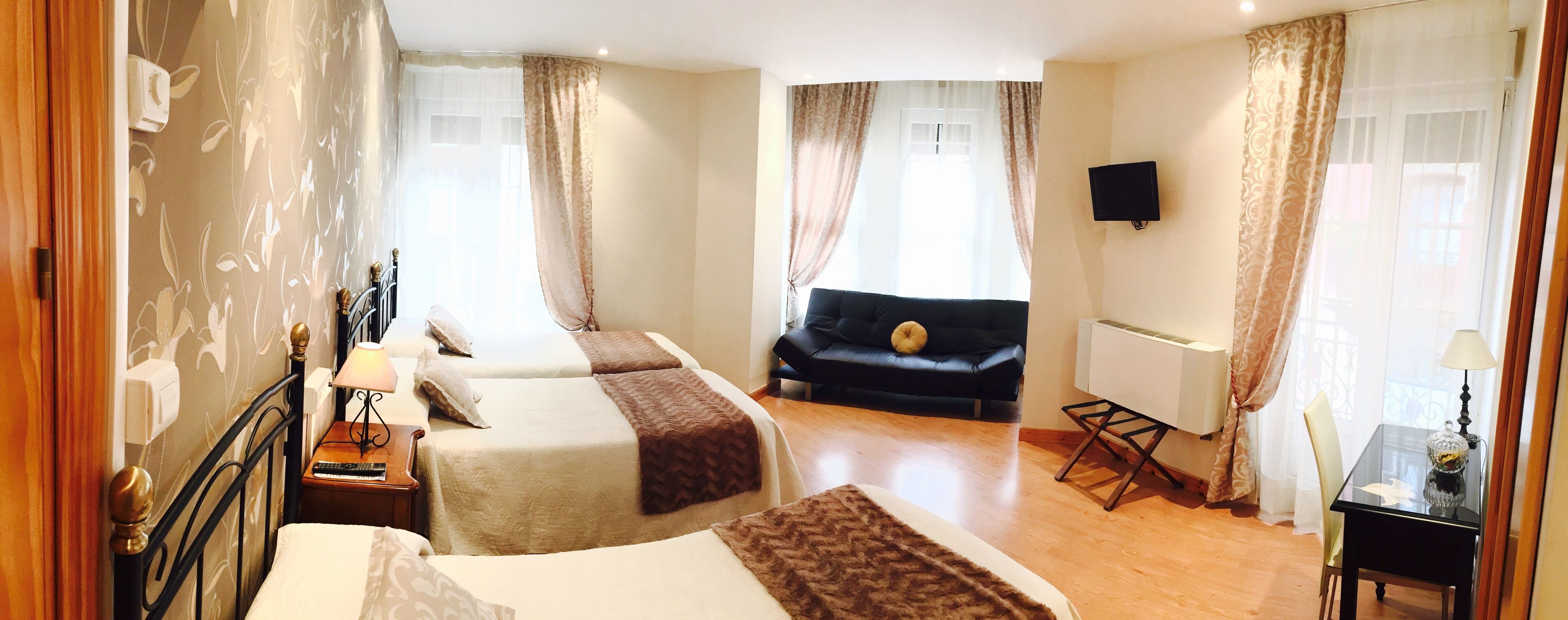 A hotel room with two beds, a sofa, a TV, and a small table with a lamp.
