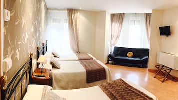 A hotel room with two beds, a sofa, a TV, and a small table with a lamp.