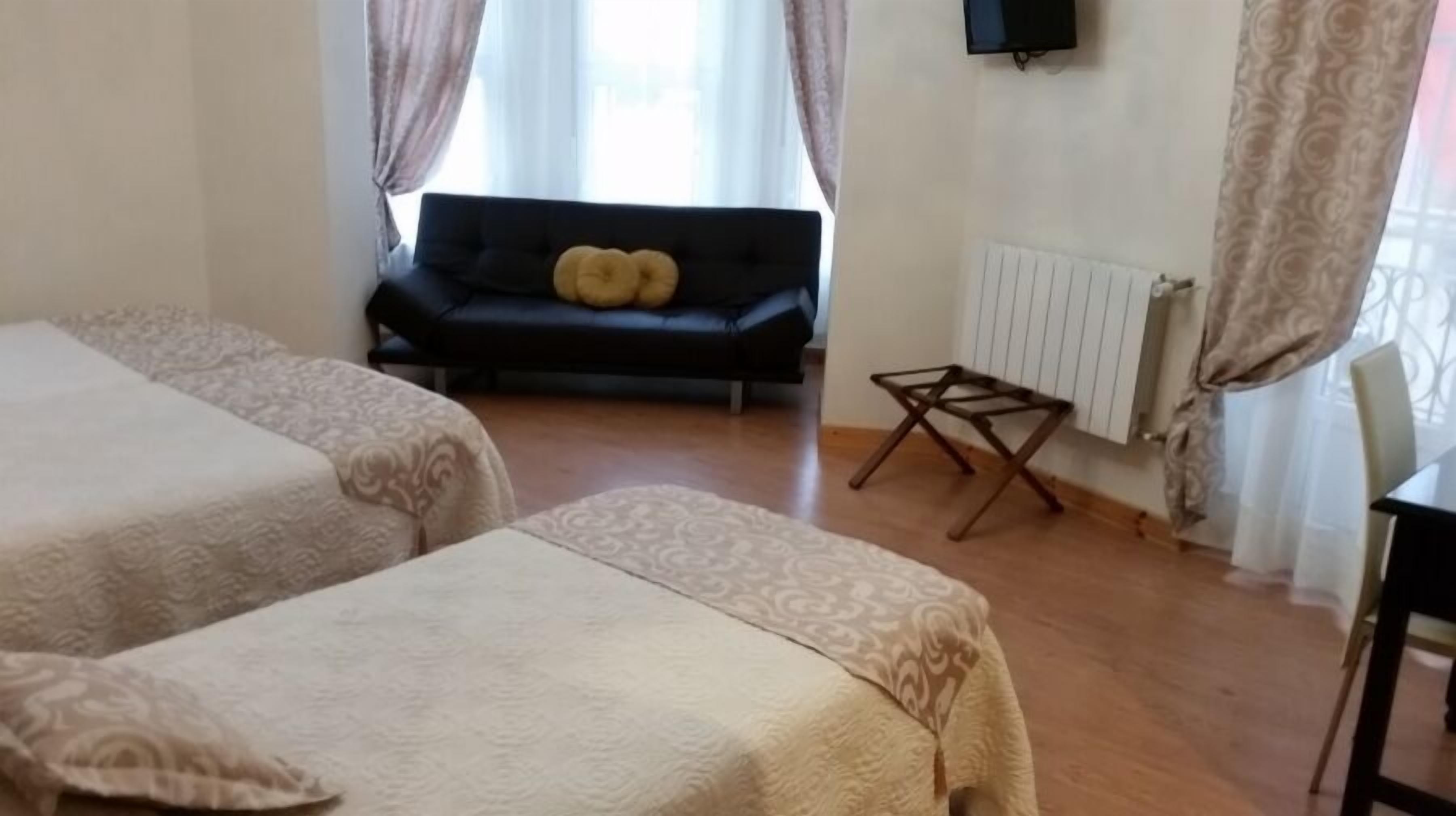 A room with two beds, a sofa, a radiator, and a TV.