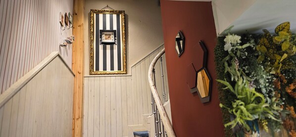 Una escalera con una pared a rayas, un cuadro enmarco y un aplique de pared.