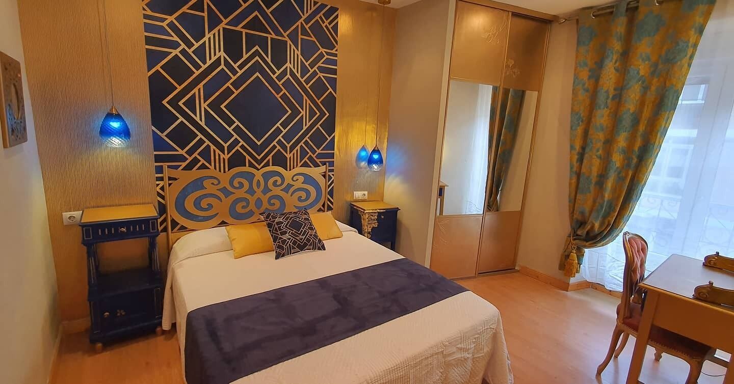 Una habitación de hotel con cama, escritorio, silla, un muro decorativo y ventana con cortinas.