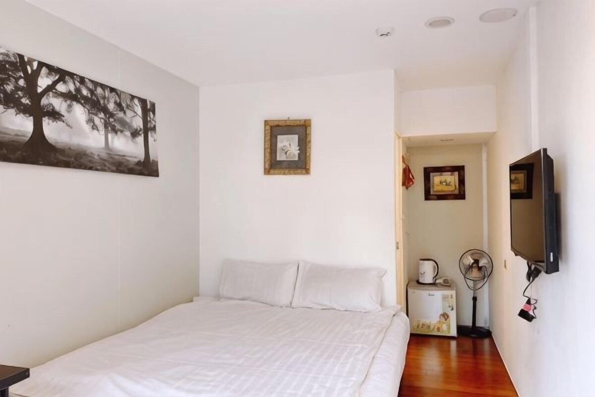 A bedroom with a bed, a wall-mounted TV, a small heater, and a picture frame on the wall.