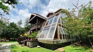 Uma casa com uma grande extensão de vidro, um deck de madeira e um caminho de pedra.