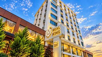 Een hotel met meerdere verdiepingen, een opvallend bord met 'Real King Suit', grote ramen en een modern architectonisch ontwerp.