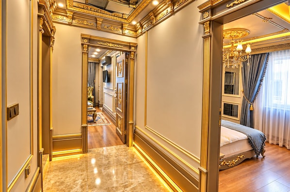 A luxurious hallway with ornate gold detailing and a marble floor leading to a bedroom with a bed and curtains. - Real King Residence (Yomra)