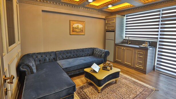 A living room with a dark blue sofa, a coffee table, and a kitchen area with a stove and cabinets. - Real King Residence  (Yomra)