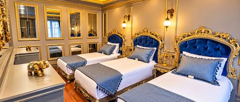Una lujosa habitación de hotel con tres camas, detalles ornamentales dorados y un espejo grande.