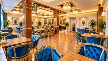 A hotel dining area with multiple tables and chairs, chandeliers, and potted plants.