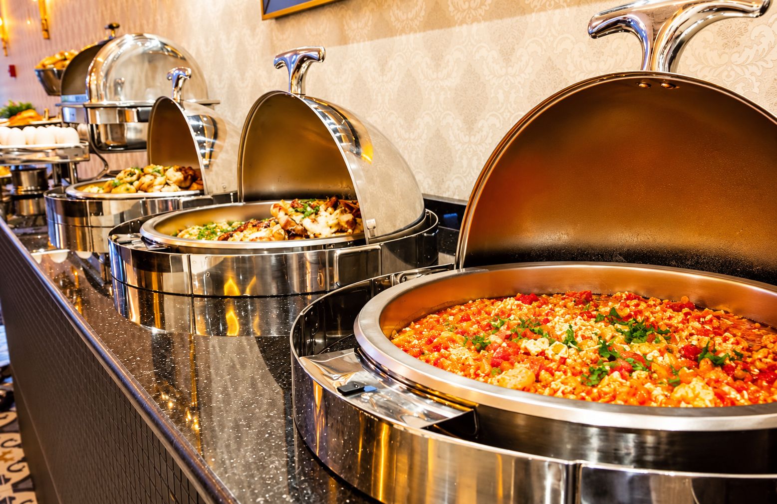 Un buffet proposant divers plats présentés dans des plats de service en acier inoxydable, dont certains sont ouverts.
