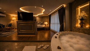 A luxurious hotel room with a large bathtub, a flat-screen TV, a sofa, and a dining area. - Real King Residence  (Yomra)