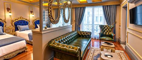 Une chambre à coucher luxueuse, avec un grand canapé vert, un fauteuil assorti, un lit doté d’une tête de lit décorée et un téléviseur fixé au mur.