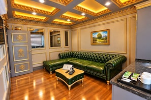 A room with a green leather sofa, a wooden coffee table with a laptop and remote control, and a painting on the wall.