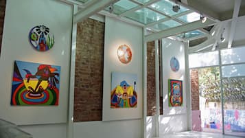 Una galería con coloridas obras de arte expuestas, un muro de ladrillo y un techo de cristal.