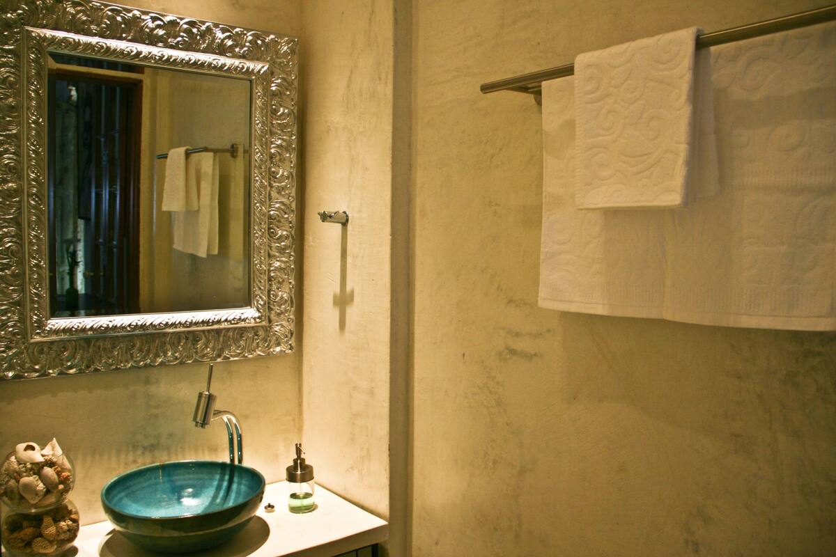 Une salle de bain avec un grand miroir décoratif, un lavabo bleu et un porte-serviettes avec deux serviettes.
