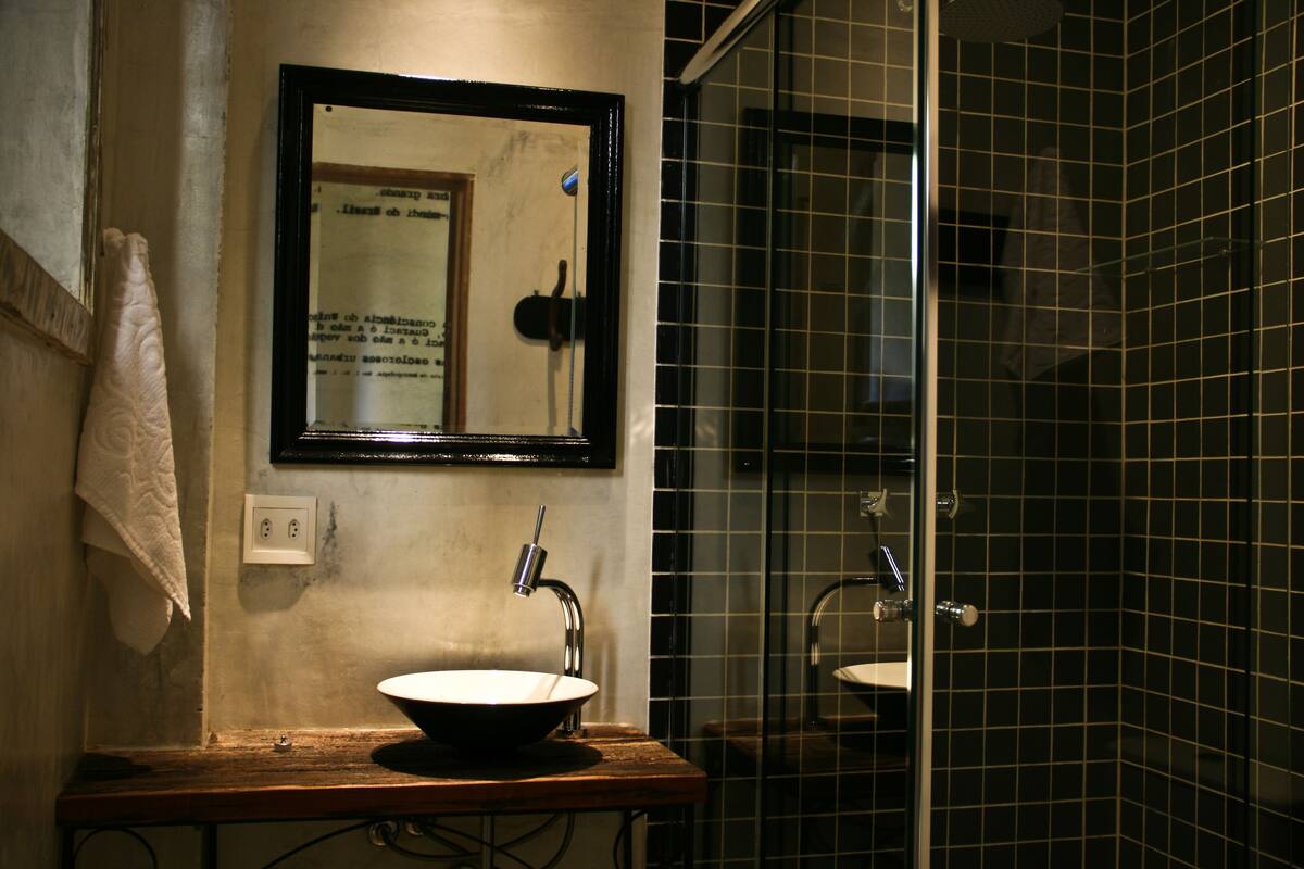 Une salle de bain avec un meuble-lavabo en bois, un évier, un miroir et un espace douche aux carreaux noirs.