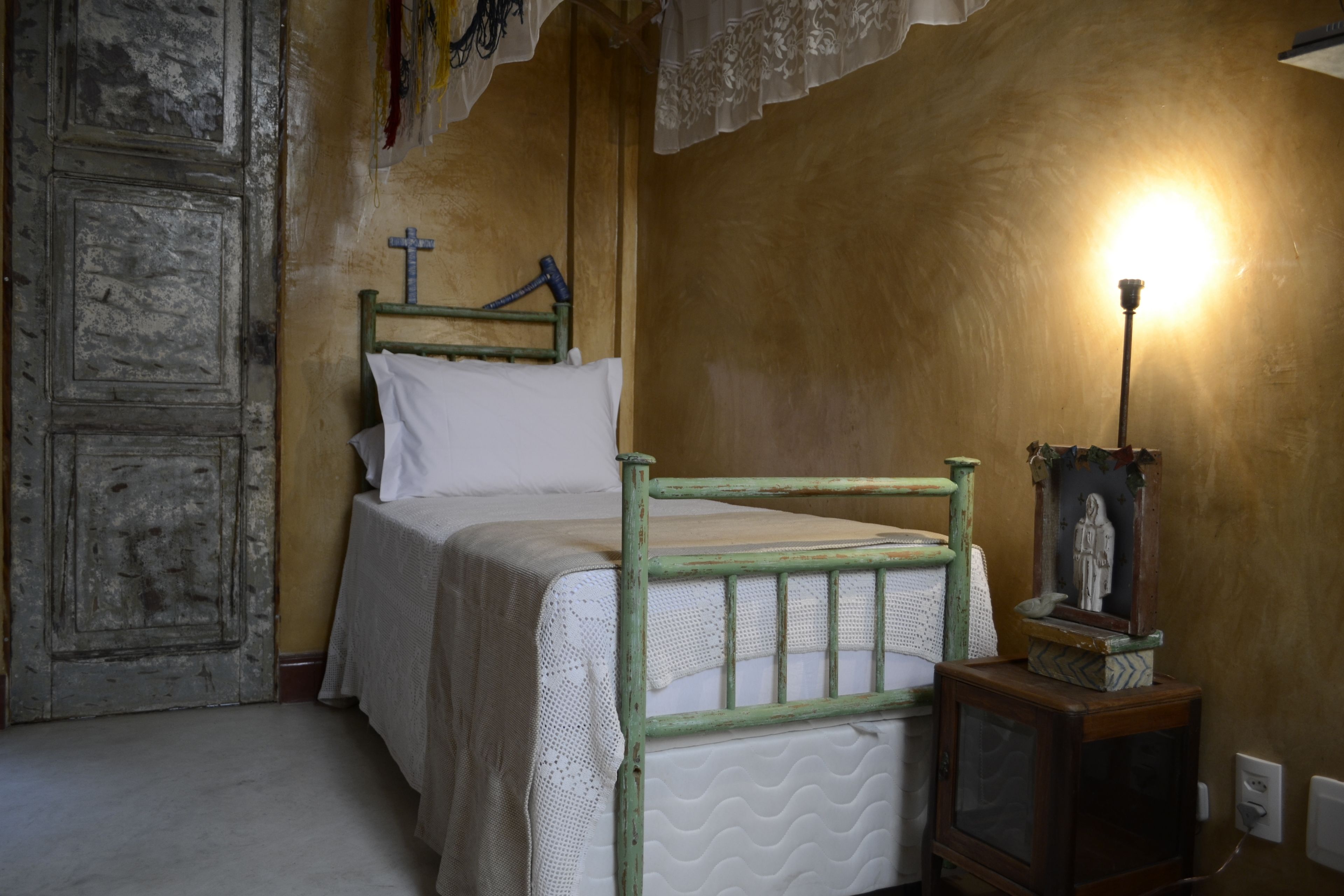 Ein Schlafzimmer mit einem hölzernen Bett, einem kleinen Nachttisch mit einer Statue und einer Wandleuchte.