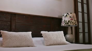 Un lit bien fait, avec du linge de lit blanc et deux oreillers blancs, une tête de lit en bois, une lampe de chevet avec un abat-jour à motifs floraux et un luminaire fixé au mur.