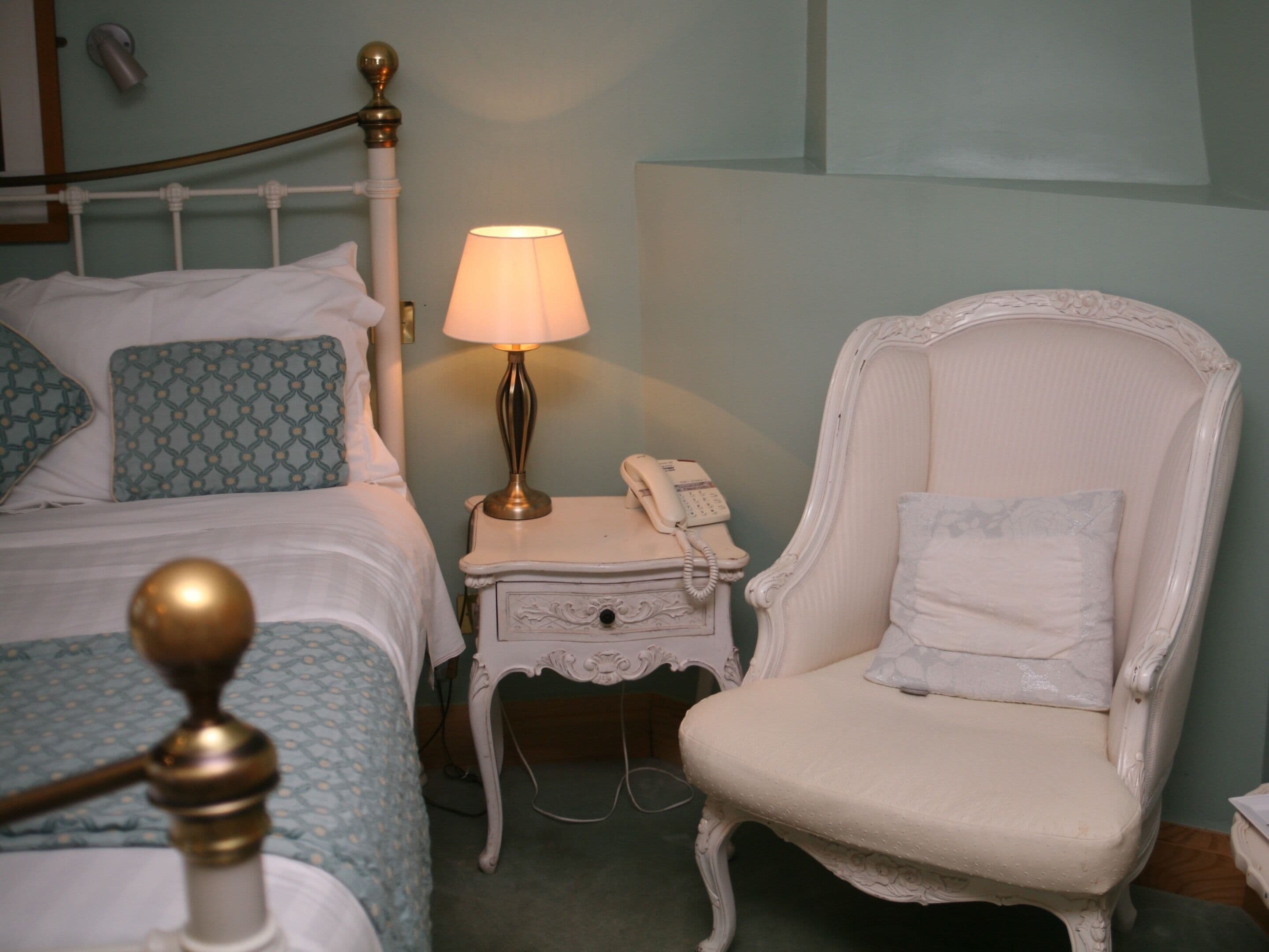 Un dormitorio con cama, una mesita de noche con lámpara, un teléfono y una silla.