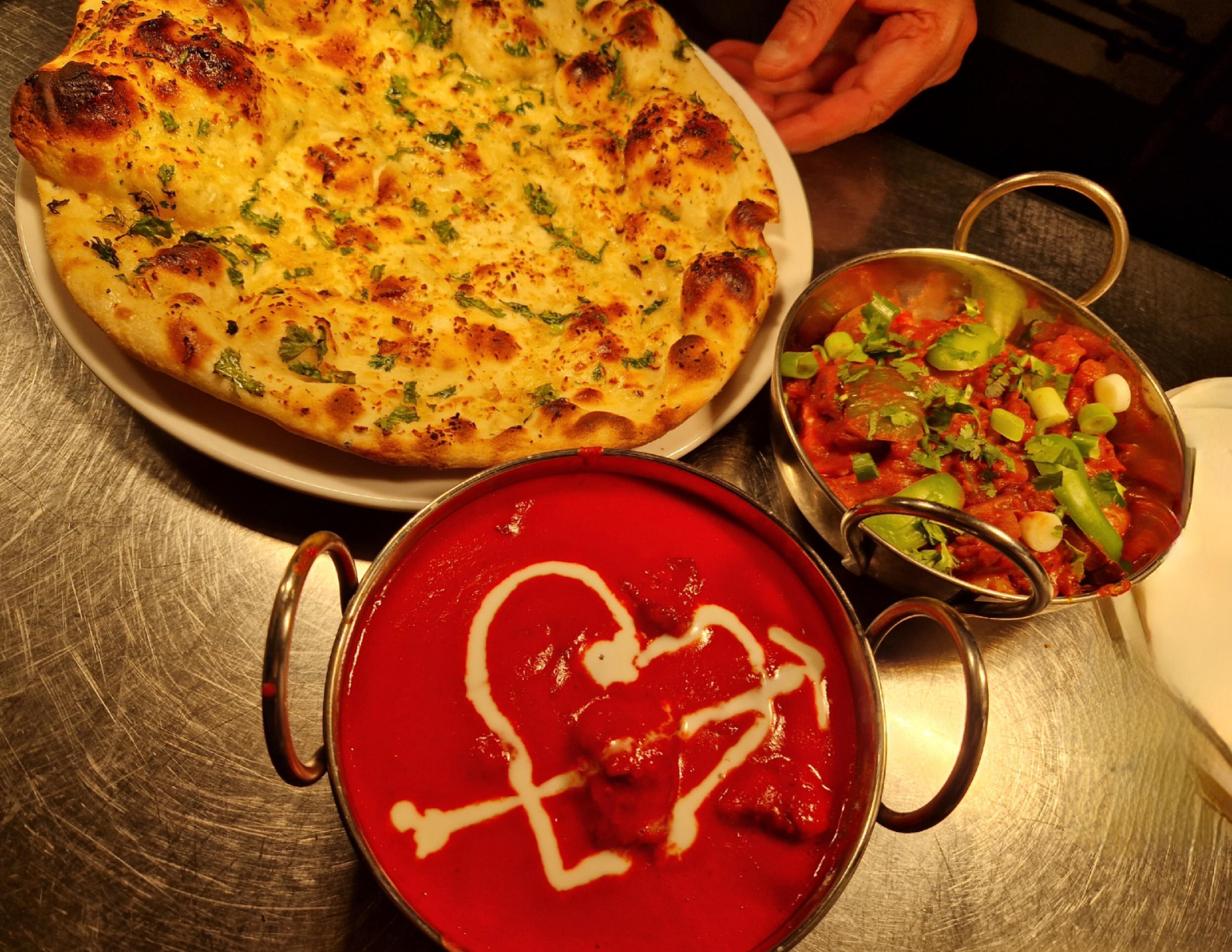 Una pizza, un tazón de sopa roja y un plato con verduras sobre una mesa.