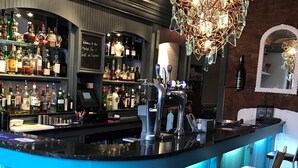 Zona de bar con mostrador, estantes llenos de botellas de licores y una lámpara colgante.