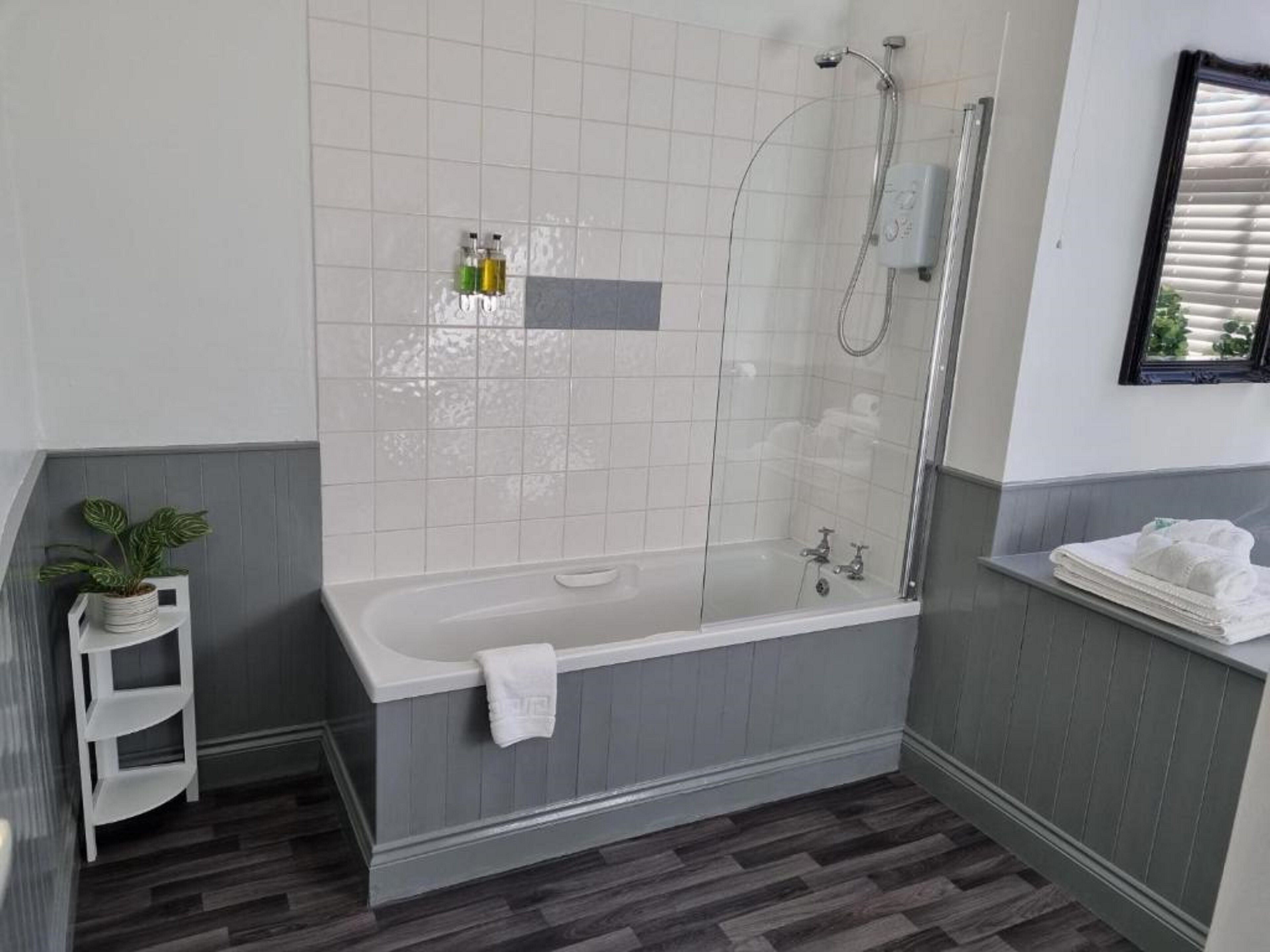 Un baño moderno con una bañera independiente, ducha con mampara de vidrio y un pequeño estante con artículos de aseo.