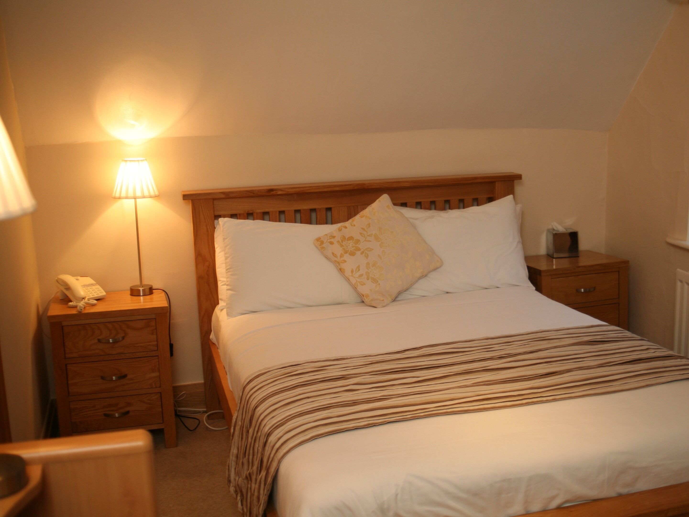 A neatly made bed with a wooden headboard, a bedside lamp, and a bedside telephone.