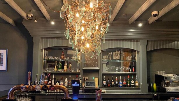 Zona de bar con una lámpara original, estantes llenos de botellas de licores y una barra con grifos.