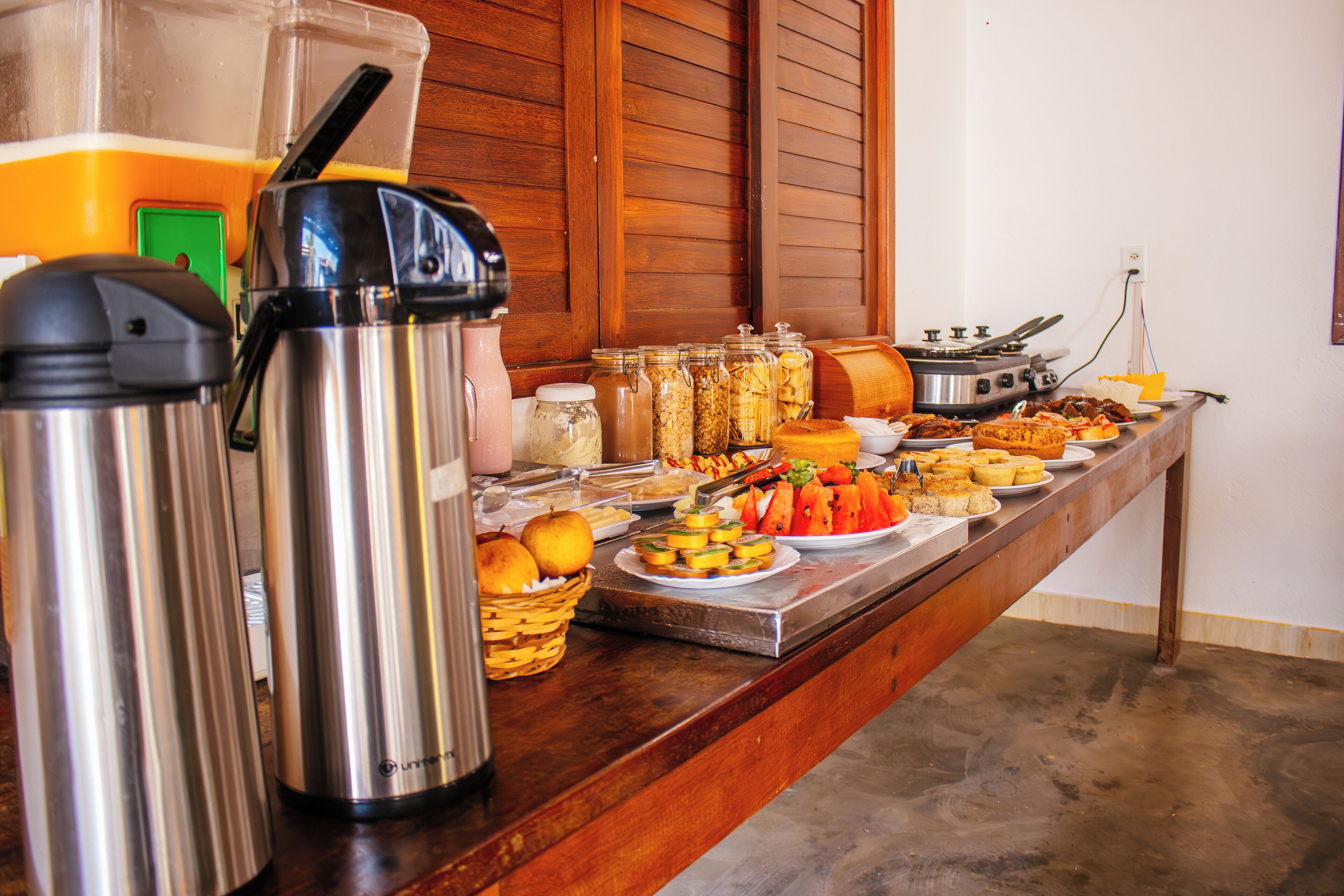 Una mesa de buffet con diversos alimentos, una cafetera y un hervidor.