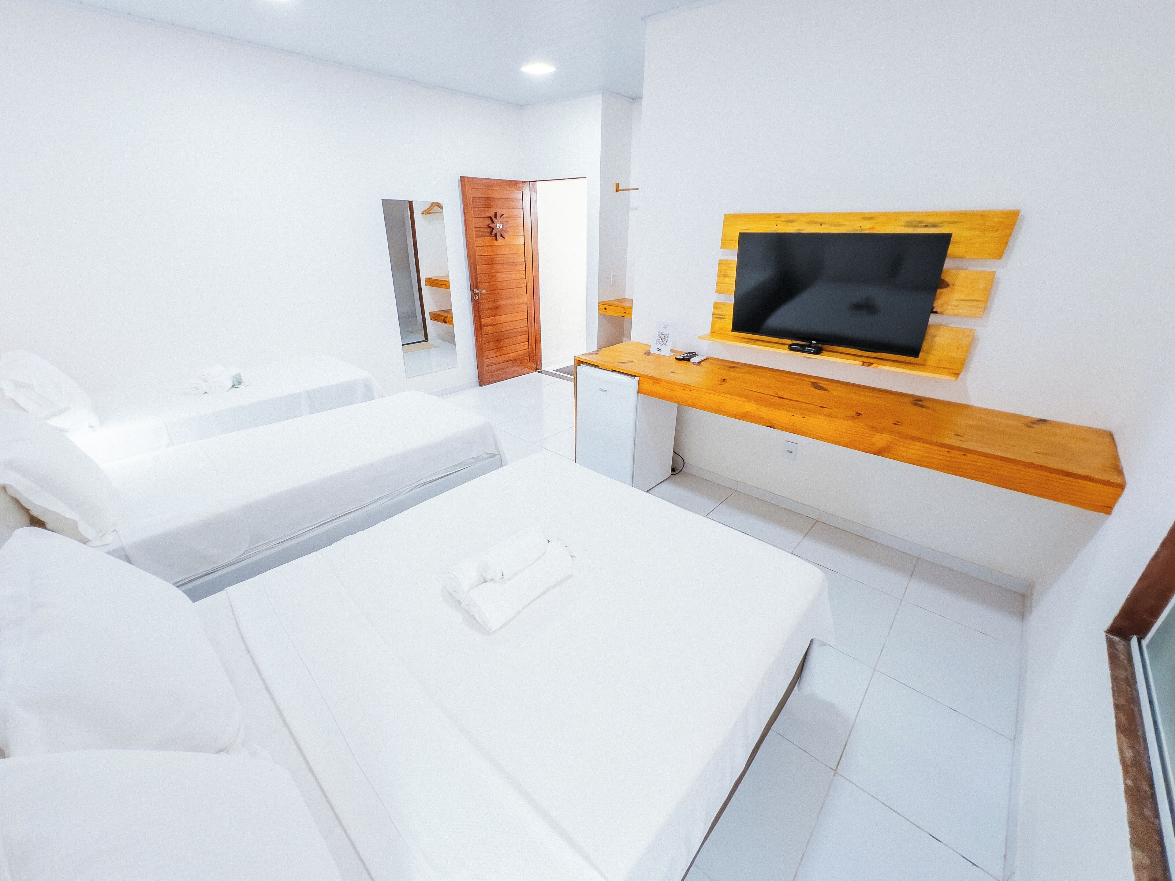 A modern hotel room with a large bed, a small seating area, a wooden TV stand, and a compact kitchenette.