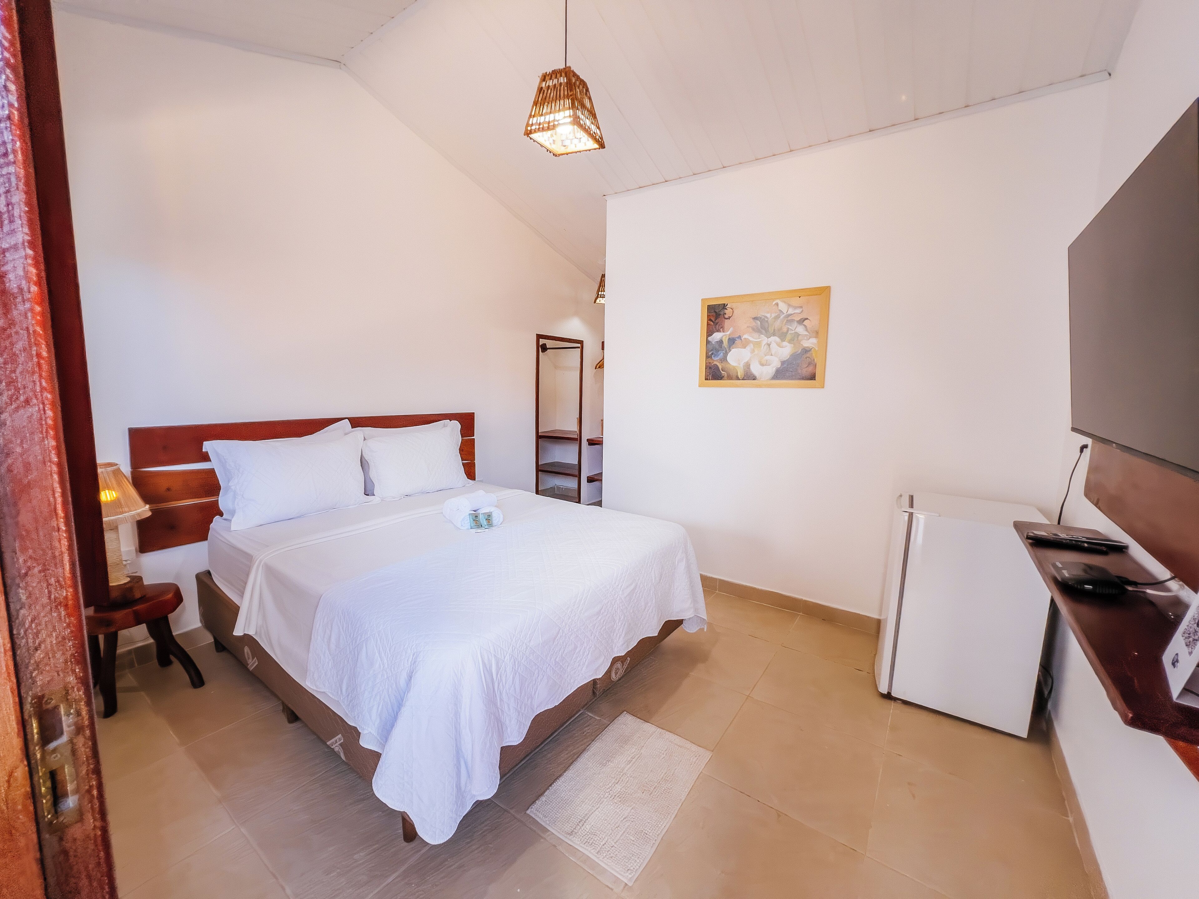 A neatly arranged bedroom with a bed, bedside table, lamp, and a small refrigerator.