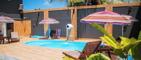 A backyard with a swimming pool, wooden deck, lounge chairs, and striped umbrellas.