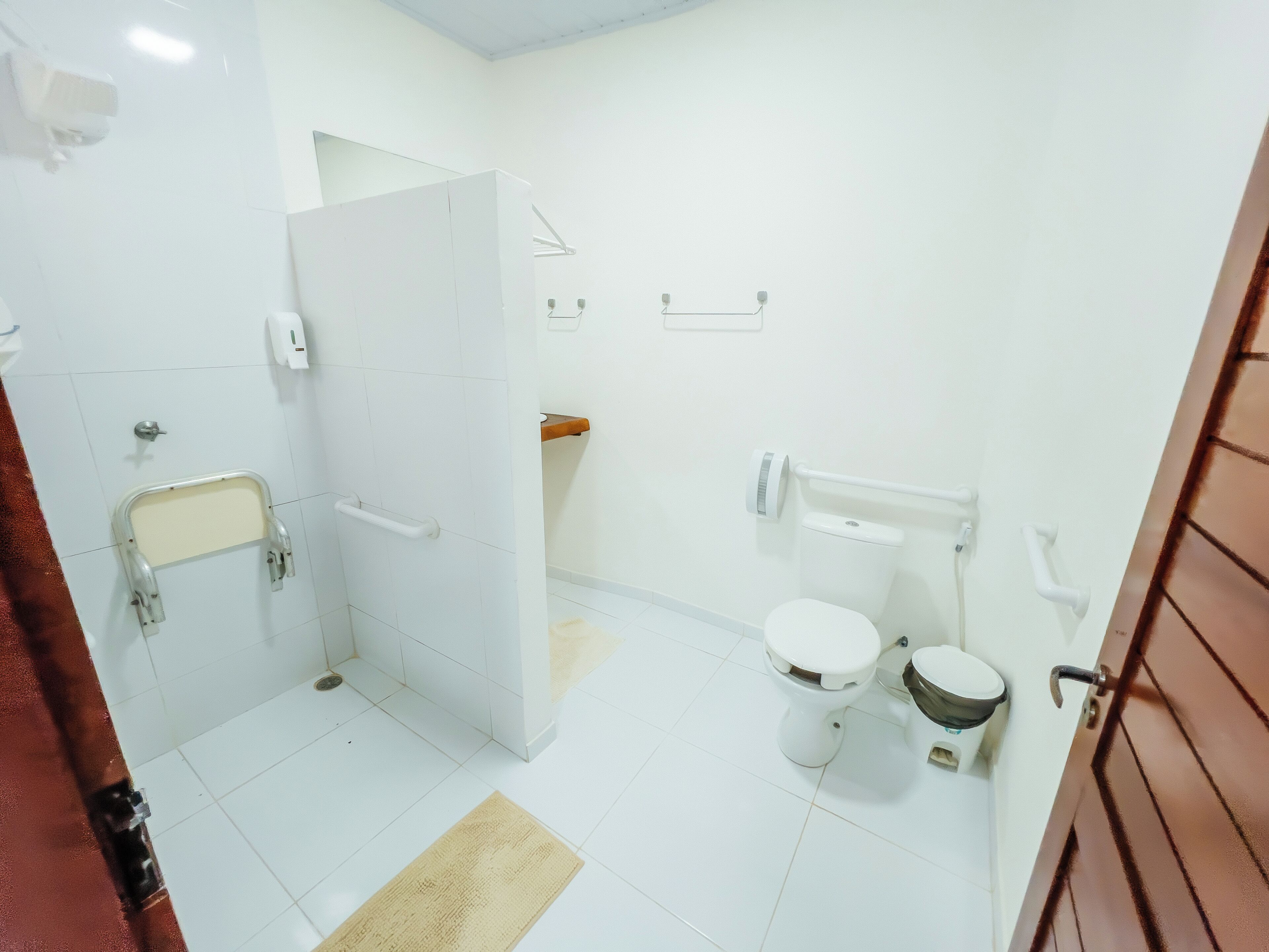 Une salle de bain avec des carreaux blancs, des toilettes, un bidet, une barre d’appui et un porte-serviettes.
