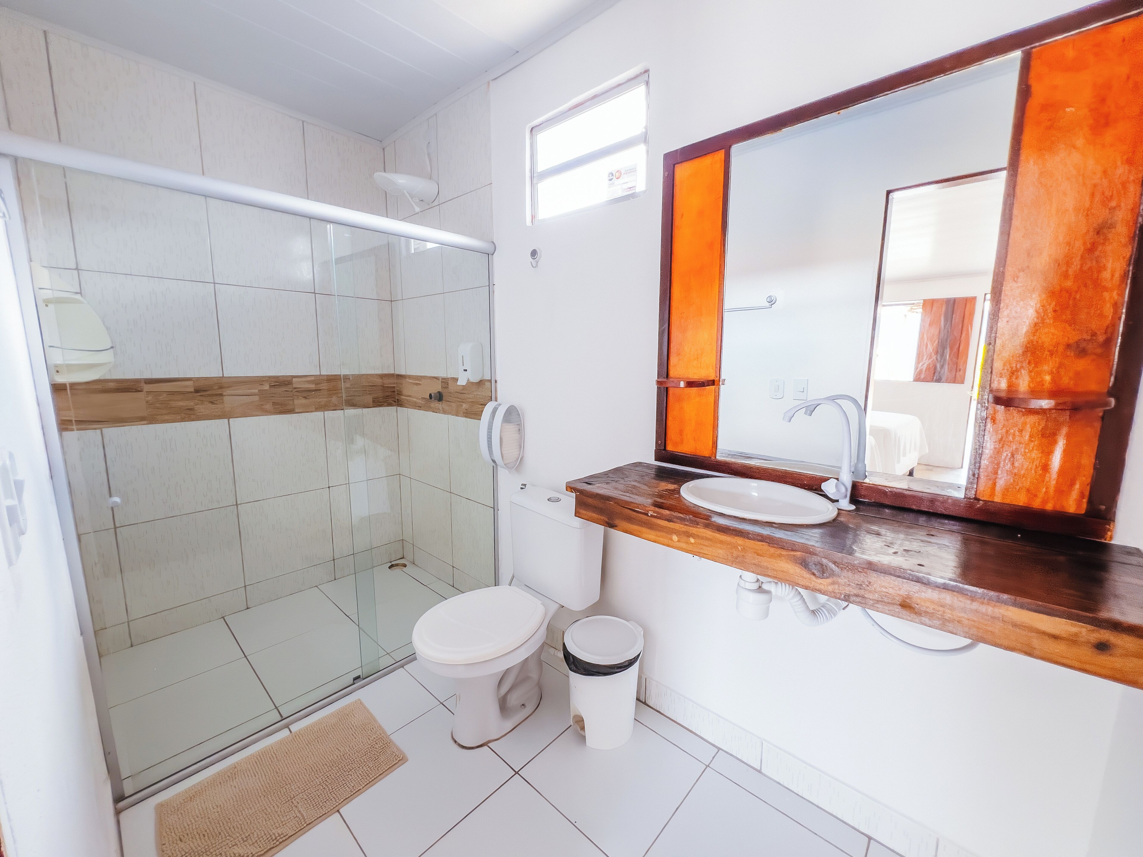 A bathroom with a glass shower enclosure, a white toilet, a sink with a wooden countertop, and a large mirror with a wooden frame.