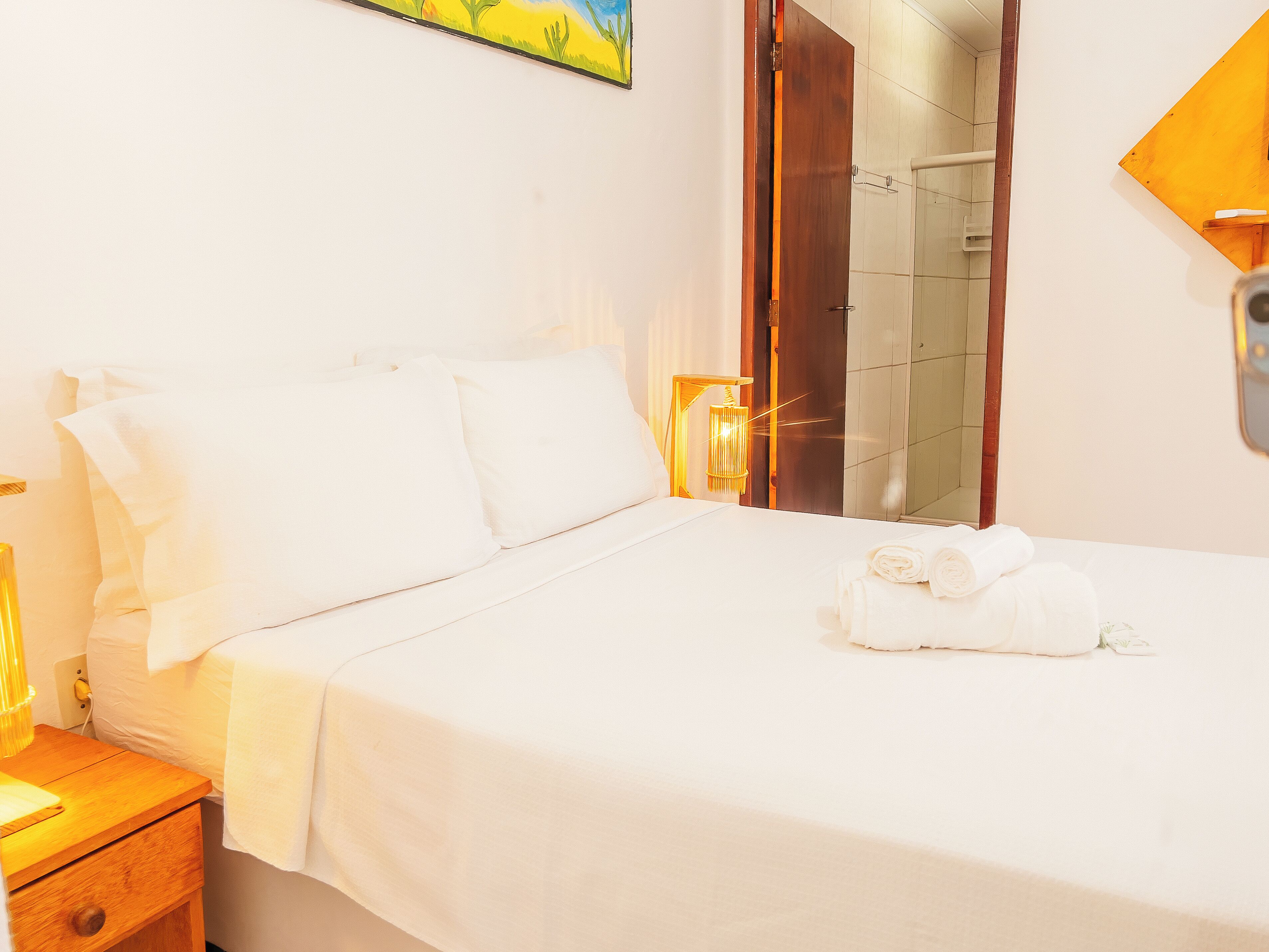 Una habitación de hotel con cama, mesita de noche, lámpara, espejo y un cuadro en la pared.