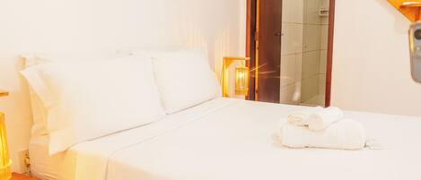 Una habitación de hotel con cama, mesita de noche, lámpara, espejo y un cuadro en la pared.