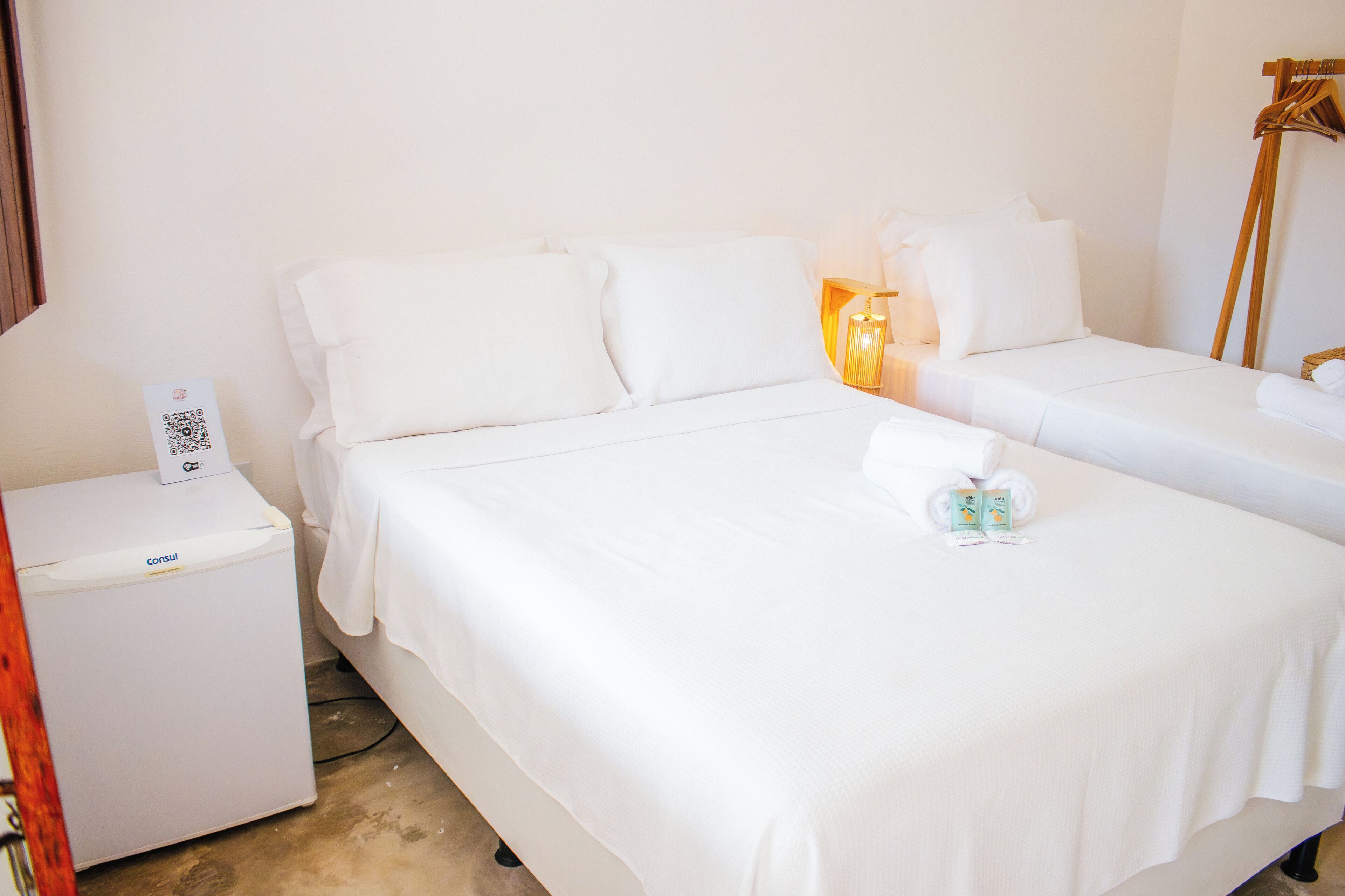 A hotel room with two beds, a bedside table with a phone, and a small table with a QR code.