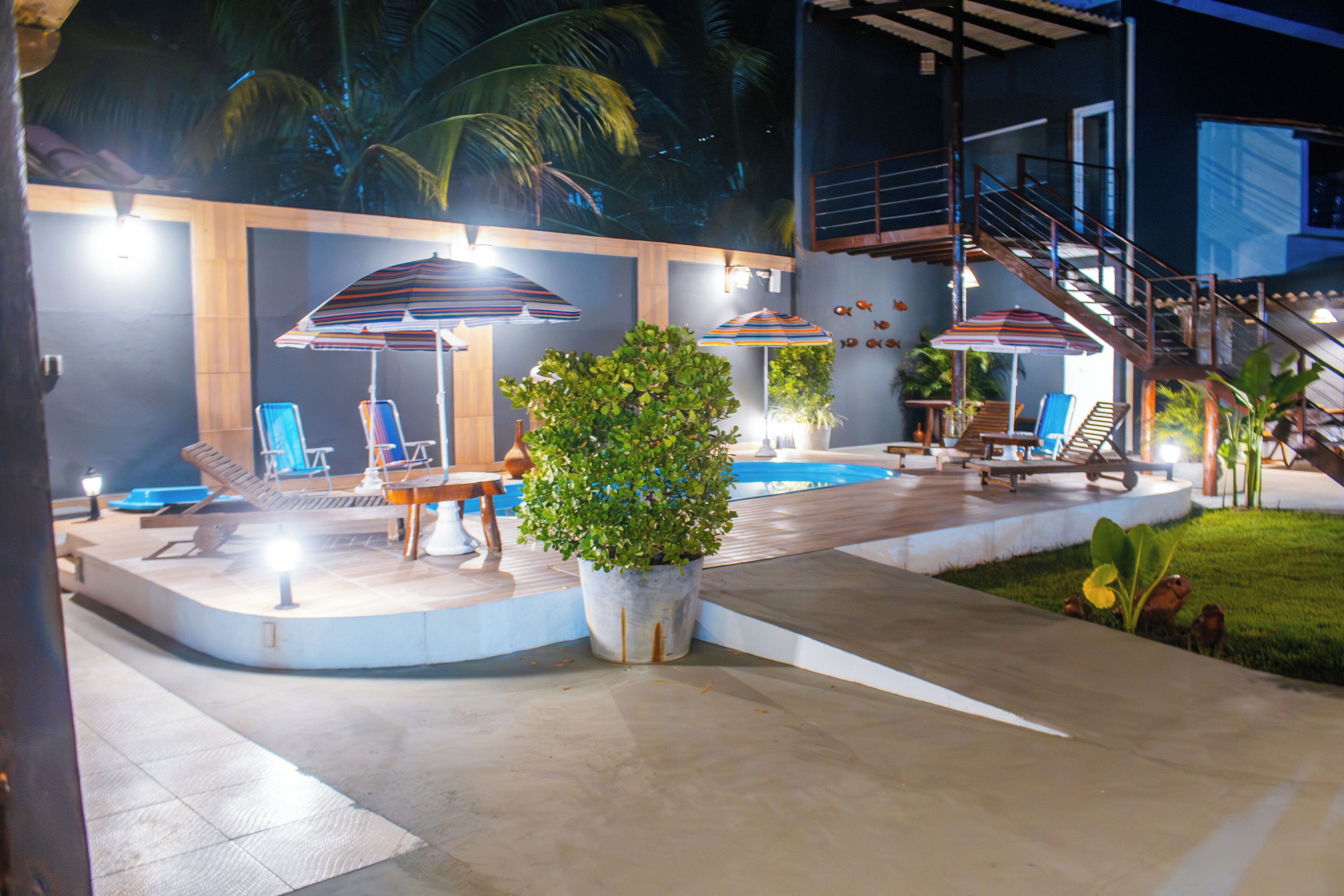 Un espace aménagé au bord de la piscine, avec des chaises longues, des parasols et un escalier menant à un niveau supérieur.