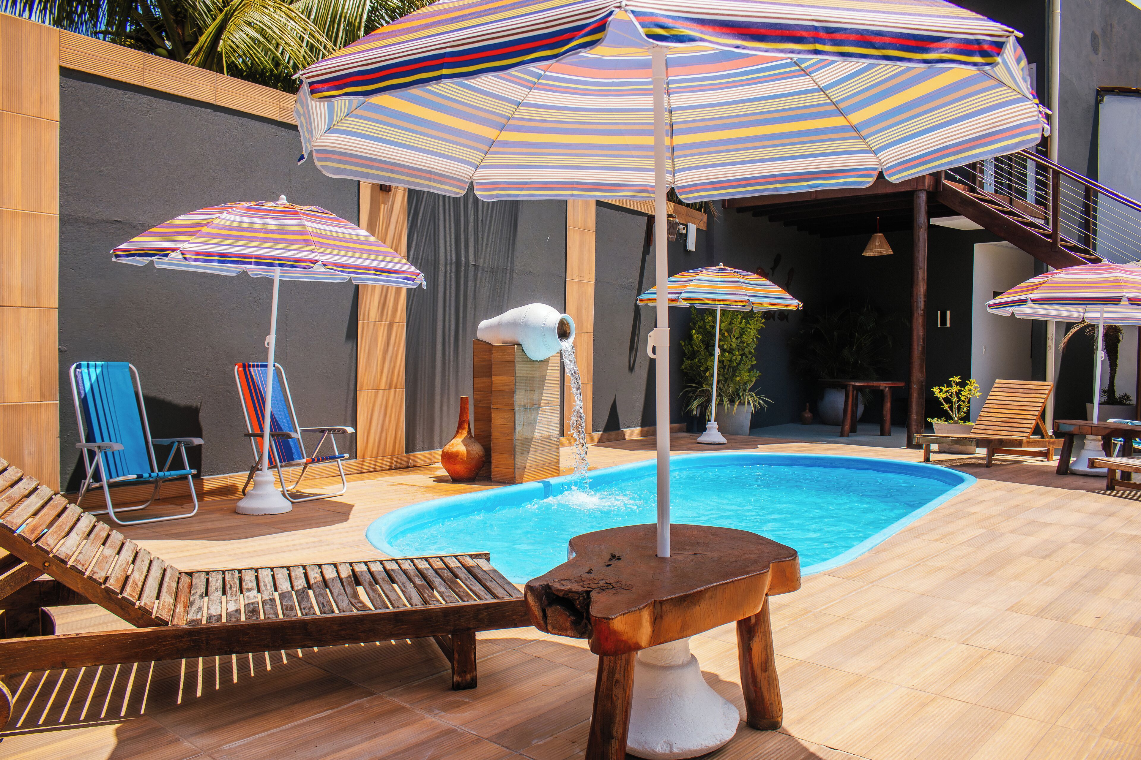 Een zwembadgedeelte met ligbedden, gestreepte parasols en een houten tafel.