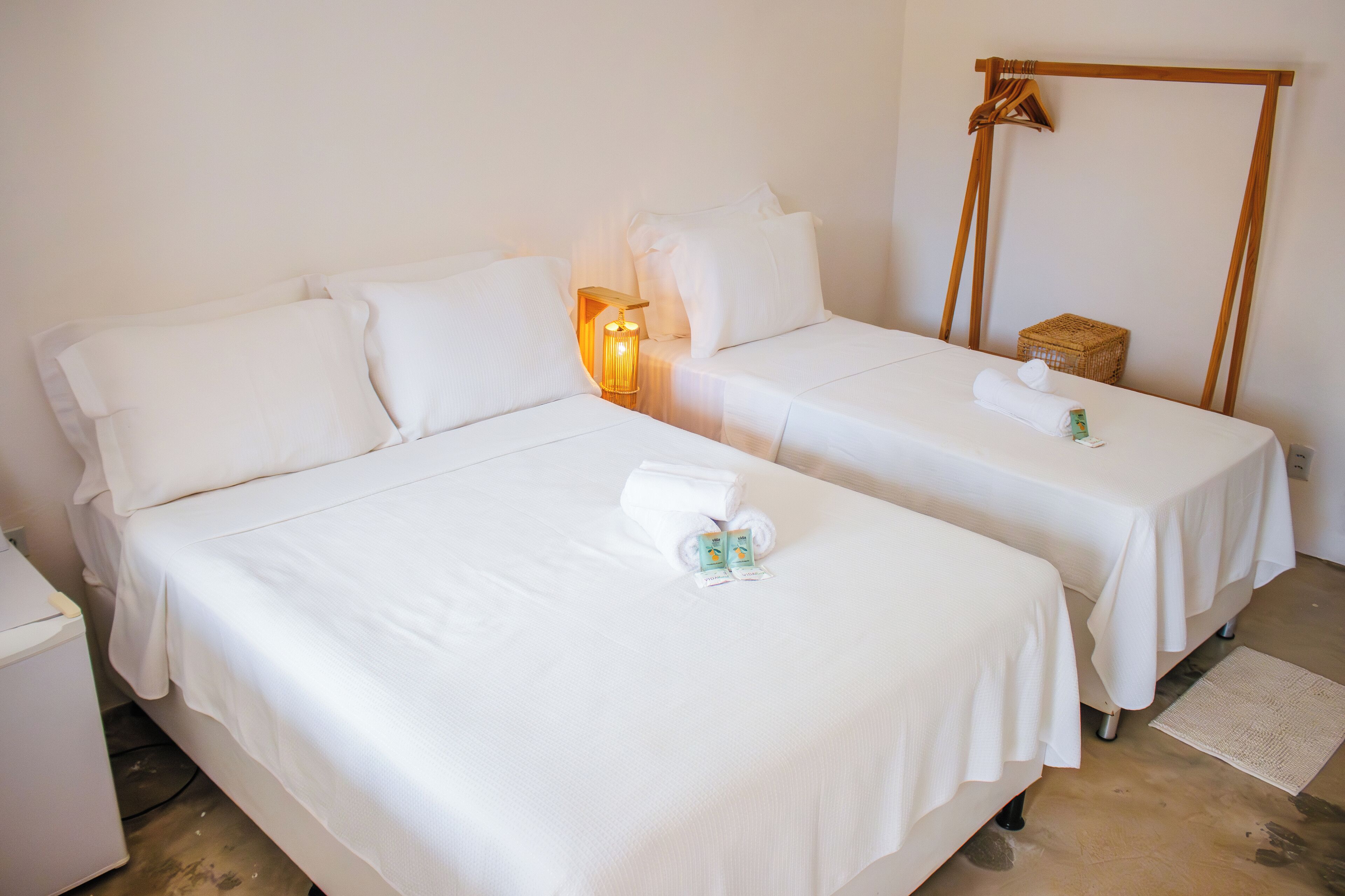 Ein Hotelzimmer mit zwei Betten, einem Nachttisch, einer Lampe, einem Handtuch und einem kleinen Korb.
