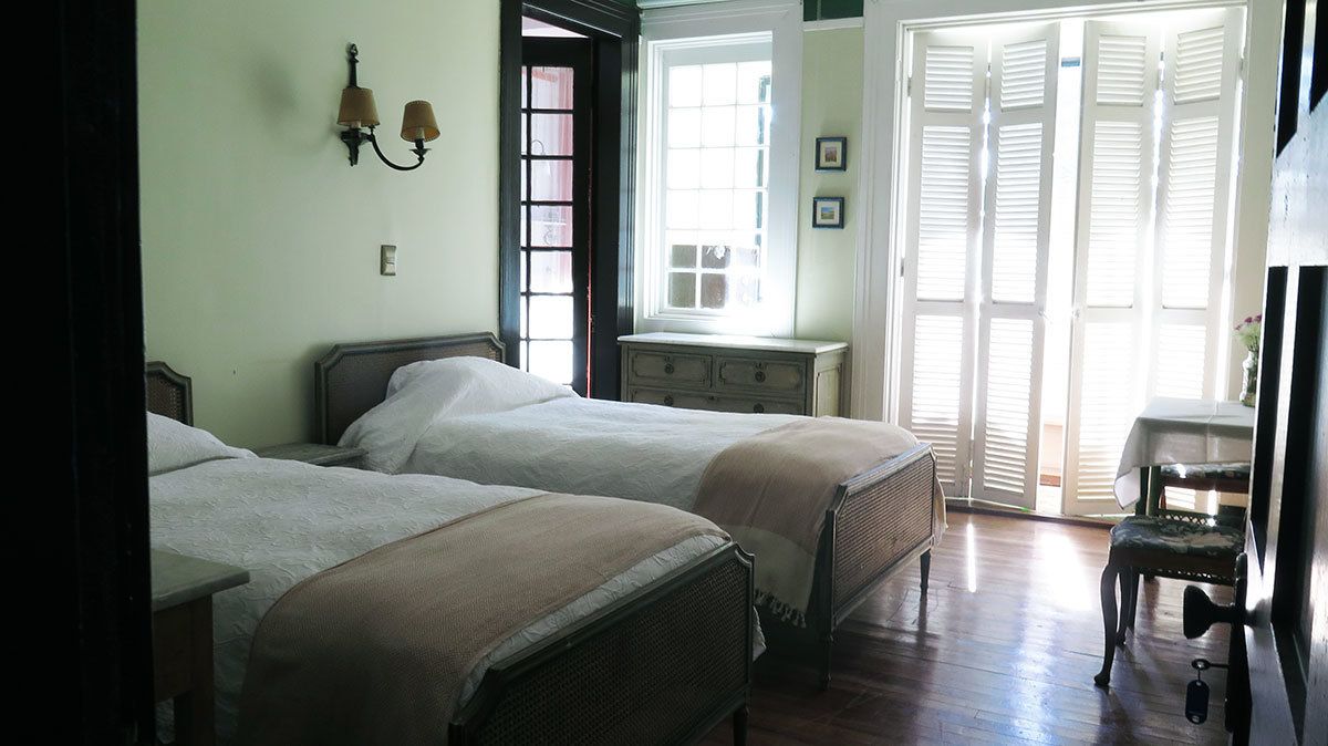 A room with two beds, a dresser, a chair, and a window with shutters.