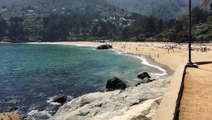 Una playa con agua turquesa cristalina, costa rocosa y colinas verdes al fondo.