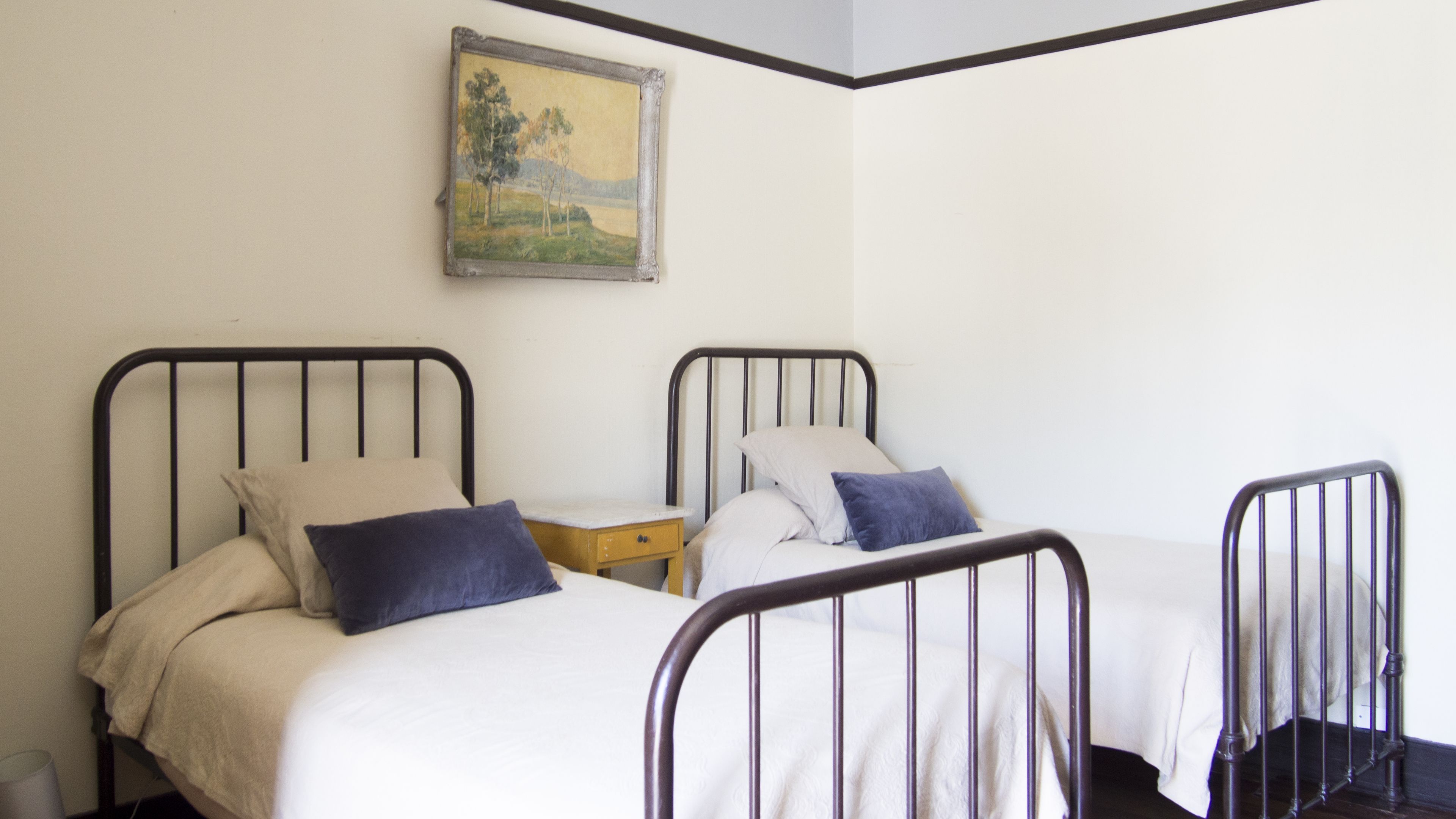 A room with two metal-framed beds, each with a pillow and a small bedside table.