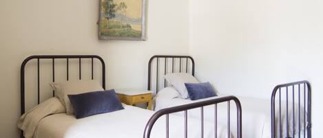 A room with two metal-framed beds, each with a pillow and a small bedside table.