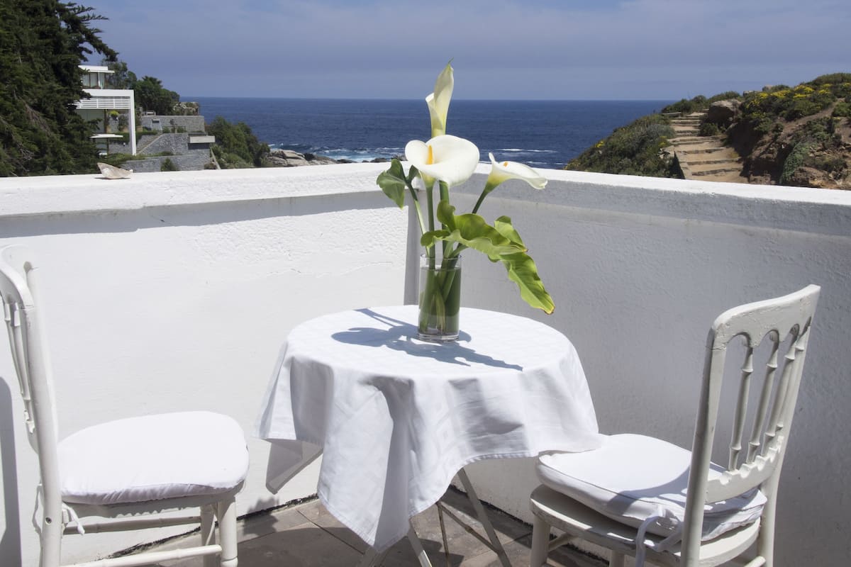 Ein Tisch mit Blumenvase, zwei weiße Stühle und Meerblick.