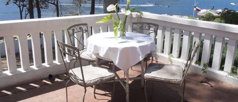 A patio with a table and chairs, overlooking a beach with boats and a flag.