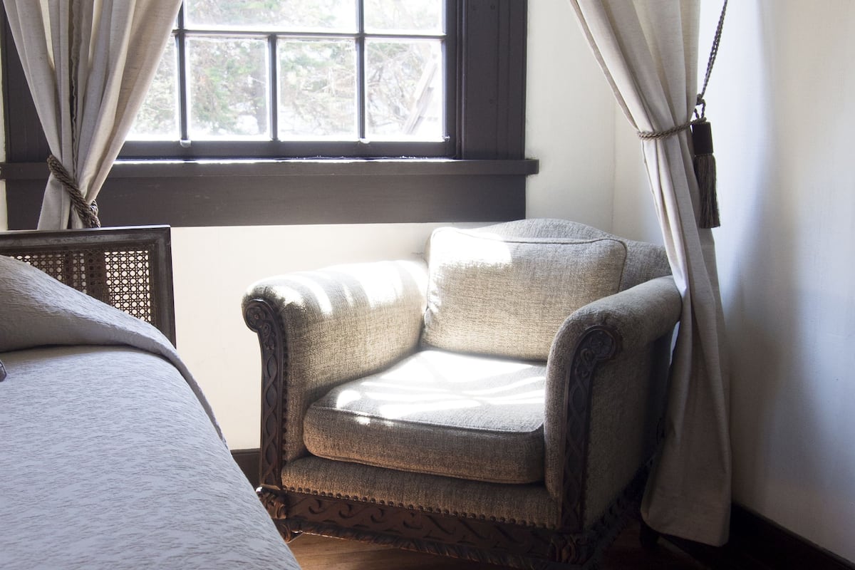 Ein Zimmer mit großem Fenster, einem Sessel und einem Bett.