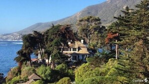 Una casa frente al mar, con vista al océano y una montaña al fondo.
