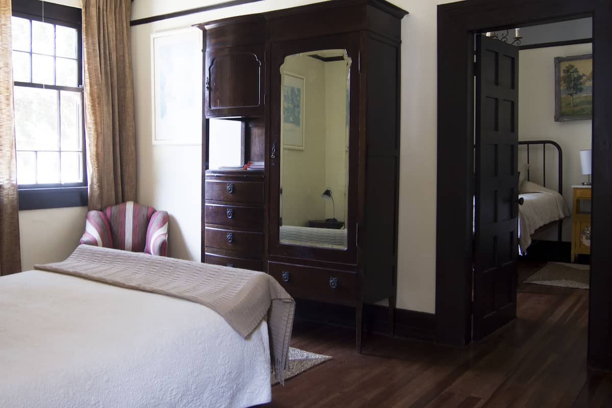 Ein Schlafzimmer mit Bett, Kommode, Spiegel und einer Tür zu einem anderen Raum.