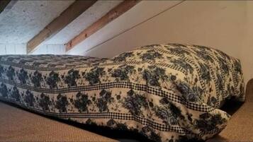 A bed with a floral patterned bedspread in a room with exposed wooden beams and a plain wall.