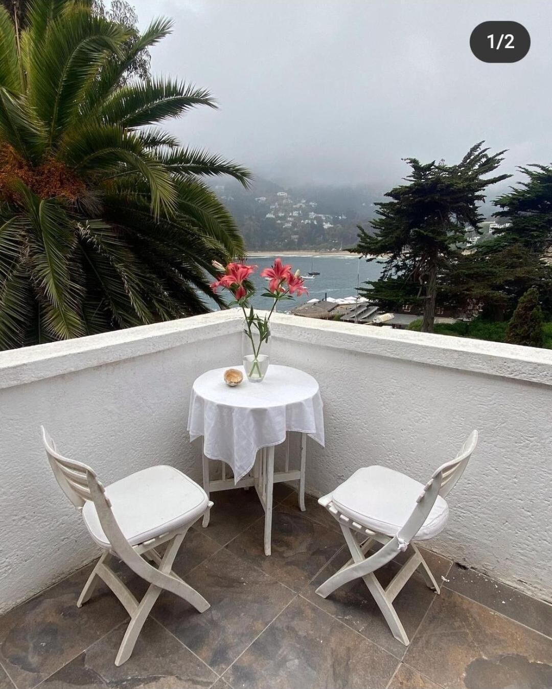 A balcony with two white chairs and a small table with a vase of pink flowers.